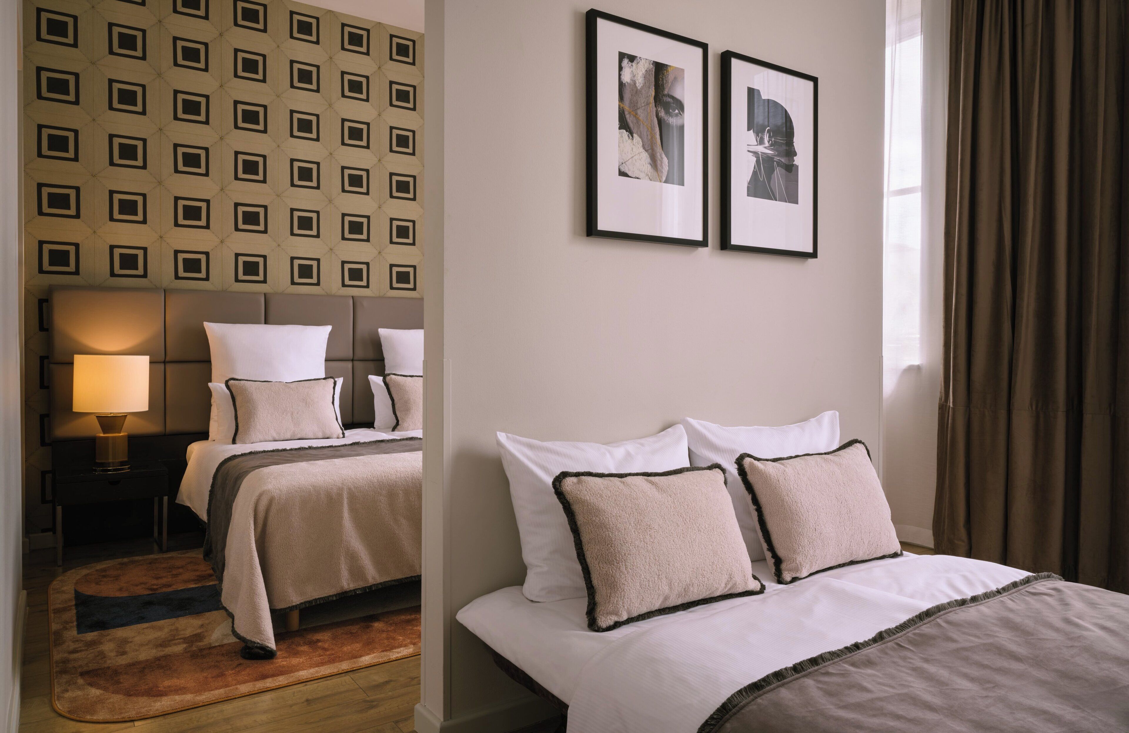Ein Hotelzimmer mit Wandmuster, einem Bett mit weißer Bettwäsche, zwei gerahmten Bildern und einem Fenster mit Vorhängen.