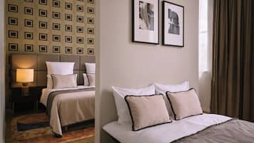 Une chambre d’hôtel avec un mur orné de motifs, un lit avec une literie blanche, deux tableaux encadrés et une fenêtre avec des rideaux.