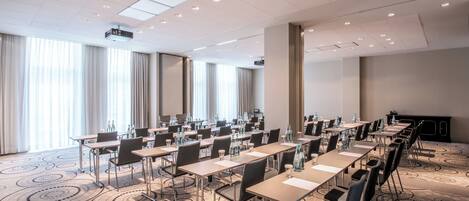 Un salón de conferencias con varias mesas, sillas y una pantalla para proyector.