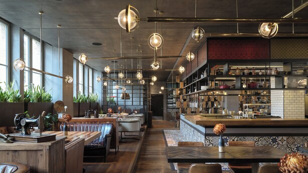 Un restaurante moderno con una barra alargada, mesas de madera y lámparas colgantes.