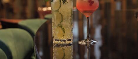 Two cocktails in glasses with mint leaves and a lime slice, placed on a reflective surface.