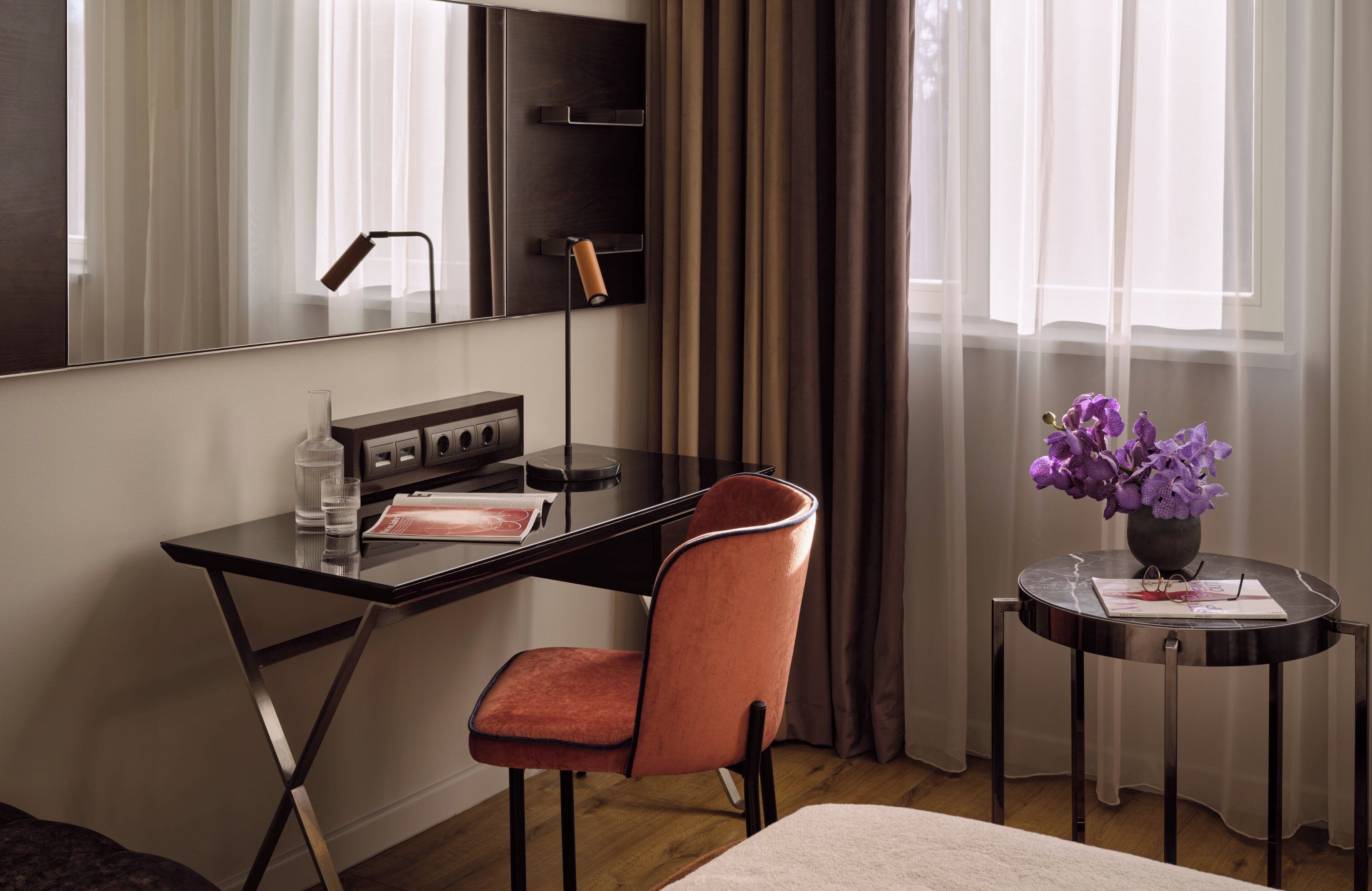 Una habitación de hotel moderna con escritorio, silla y una mesita con un florero.