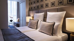 Habitación de hotel con una cama grande, dos lámparas de noche, un cabecero con diseño geométrico y vistas a un balcón con una planta.