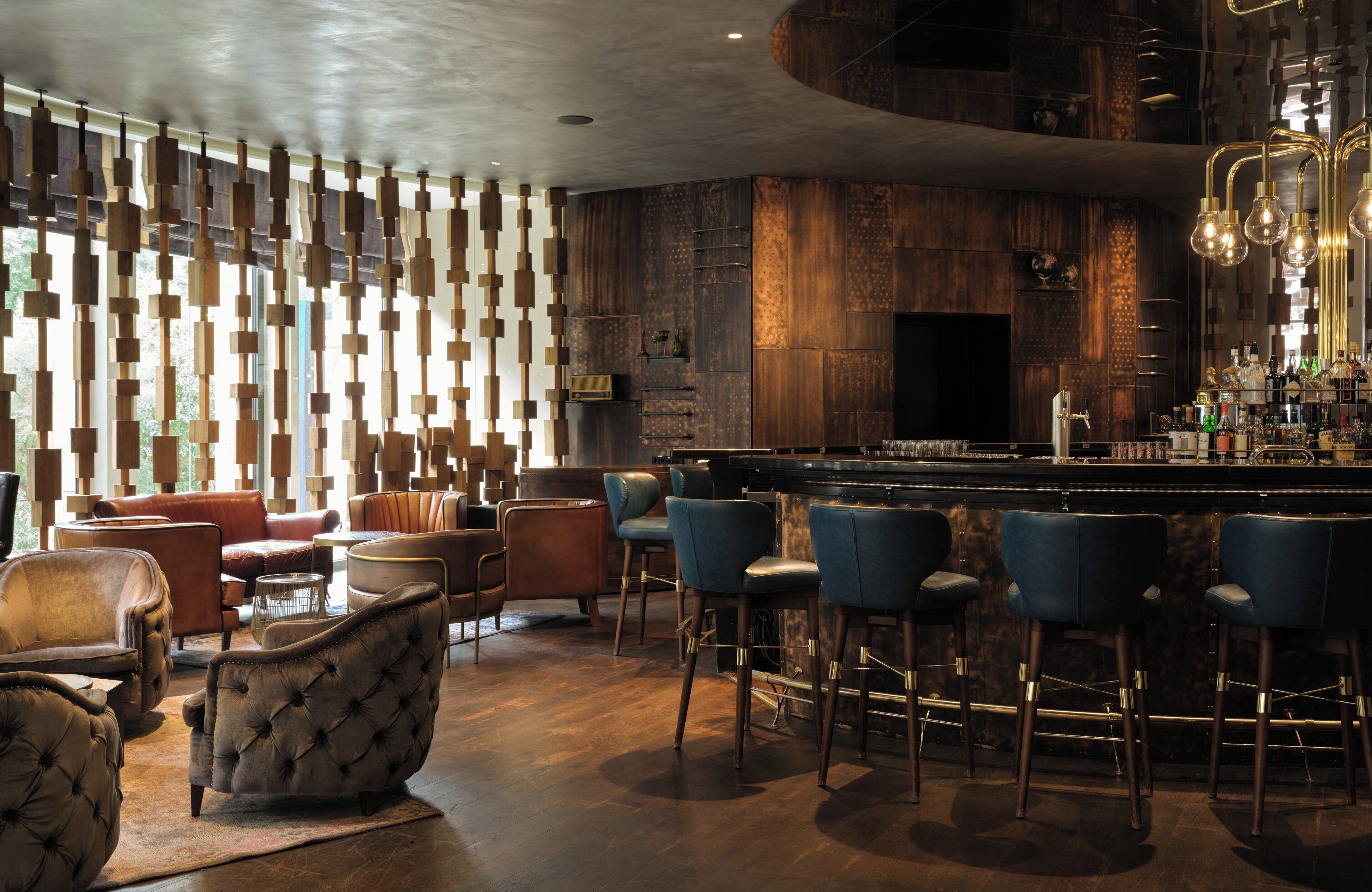A bar area with leather chairs, a bar counter, and a wooden wall with hanging lights.