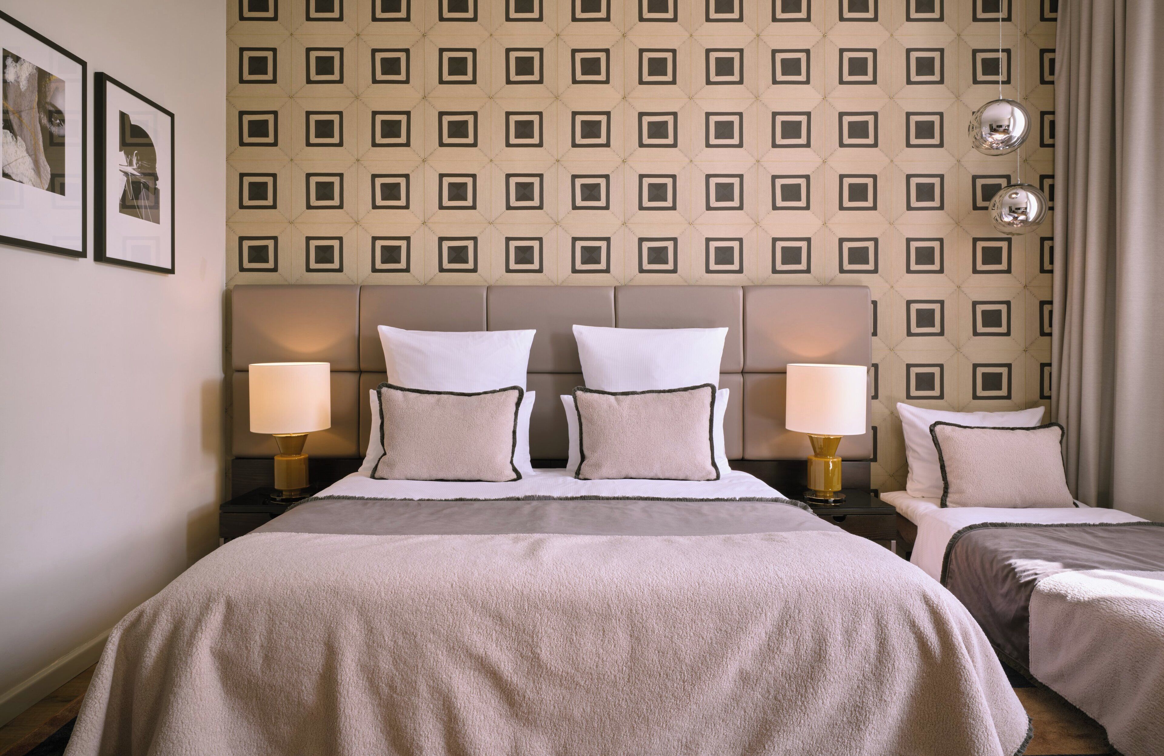 A hotel room with a large bed, two bedside tables, two lamps, and a patterned wallpaper.