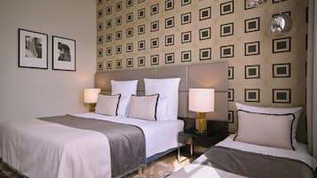 Habitación de hotel con dos camas, un papel tapiz estampado, obras de arte enmarcadas y una mesita de noche con lámpara.