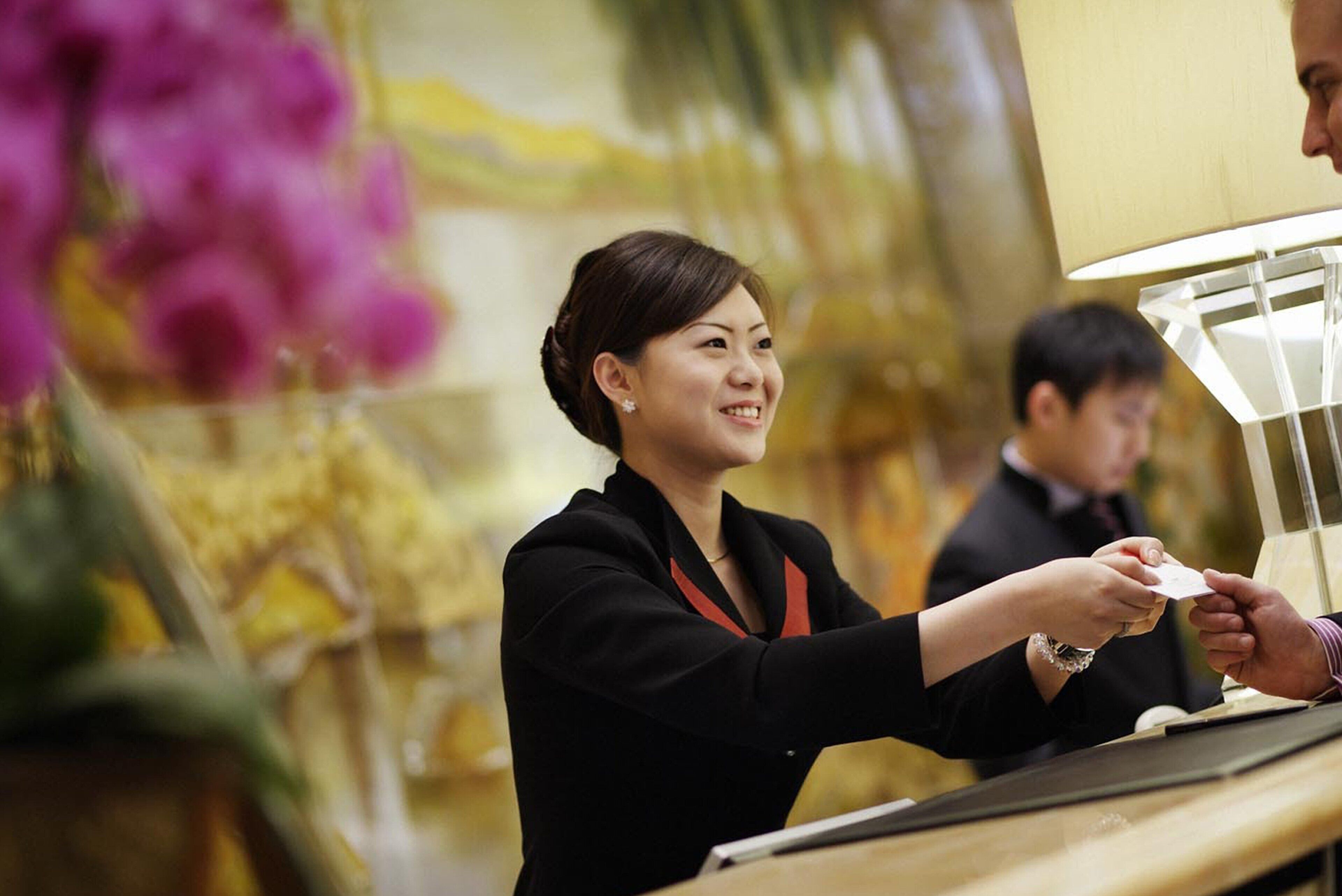 A hotel reception area with a counter and a person handing over a card to another individual.