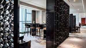 A modern hotel lobby with a geometric black partition, a bar area with stools, and a stone-patterned floor.