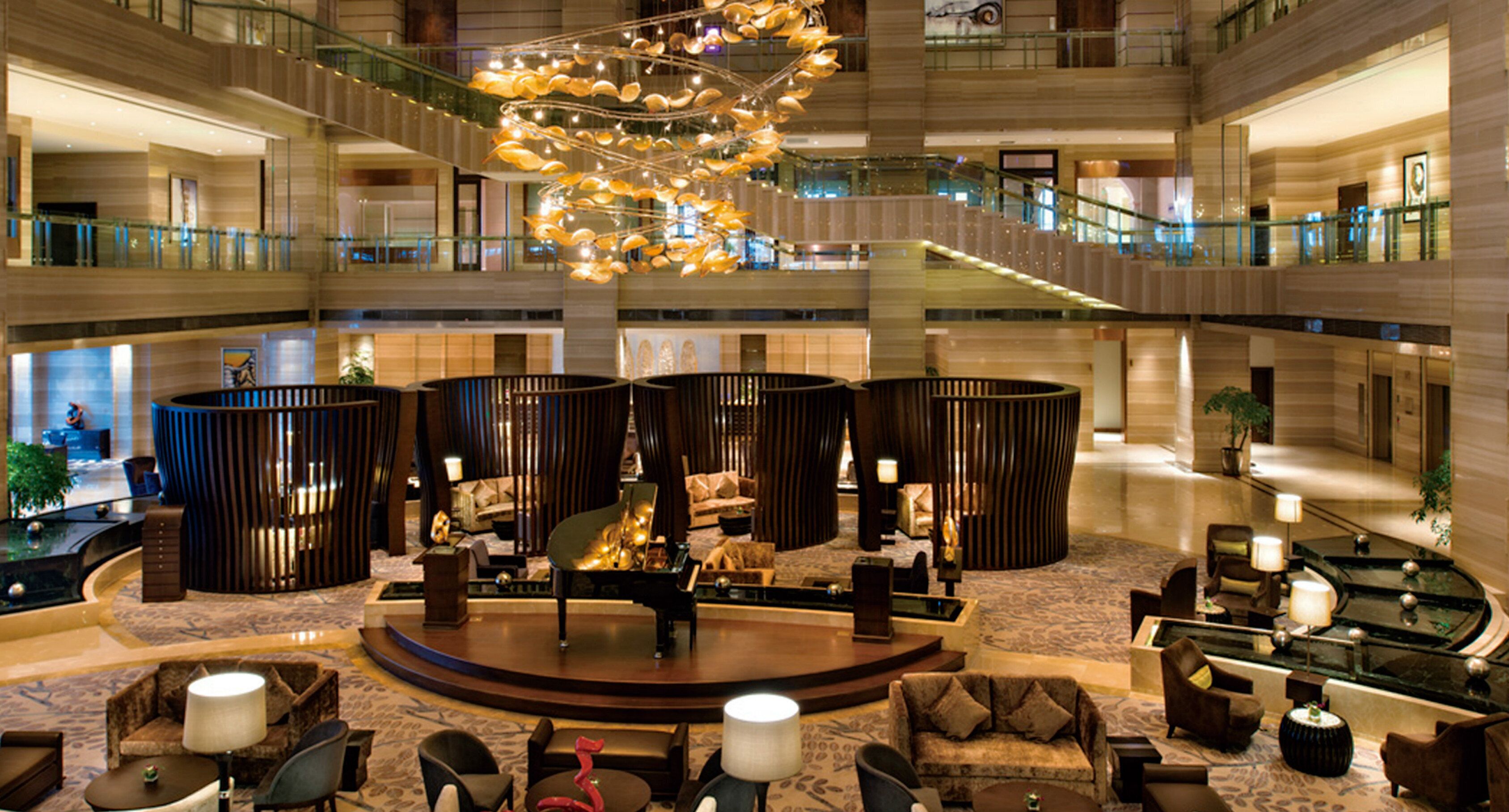 A spacious lobby with a central seating area, multiple levels, and a modern chandelier.