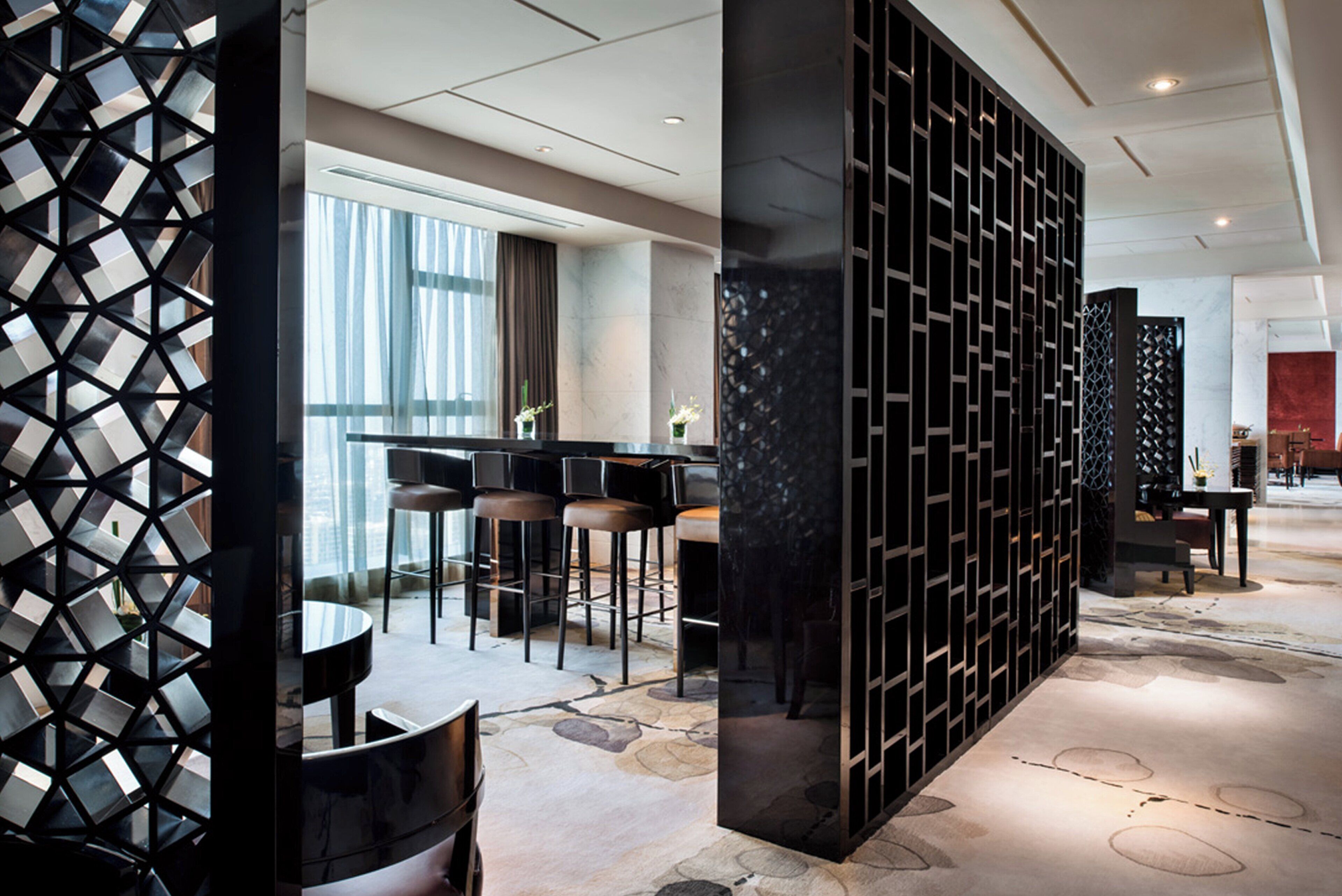 Un moderno vestíbulo de hotel con área de bar, asientos y una partición decorativa negra.