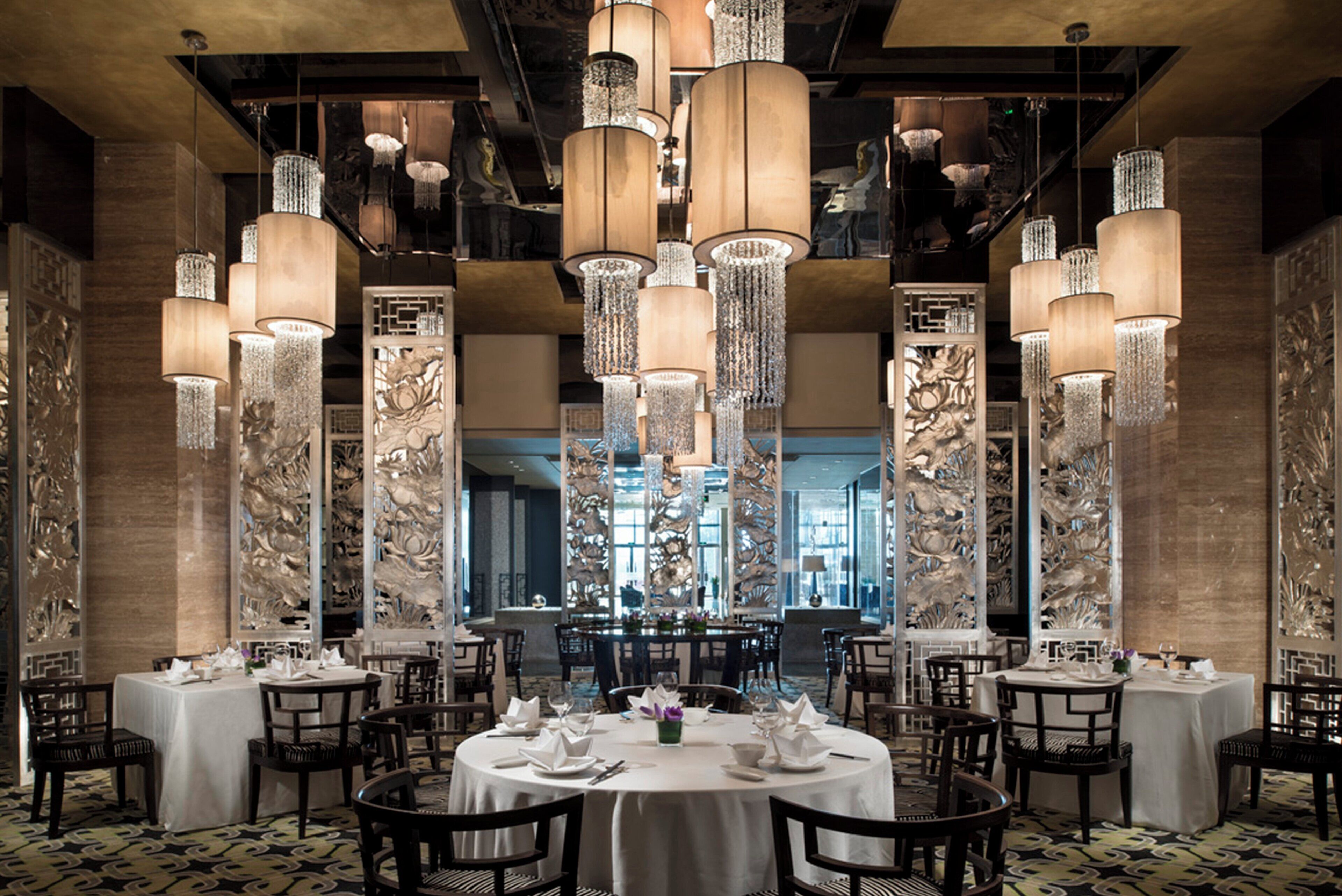 Un restaurante con mesas redondas, candelabros en el techo y paneles decorativos en las paredes.