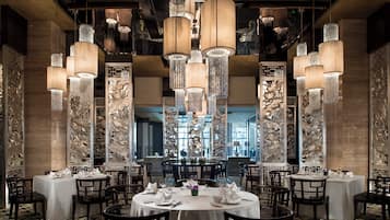 Un restaurante con mesas redondas, candelabros en el techo y paneles decorativos en las paredes.