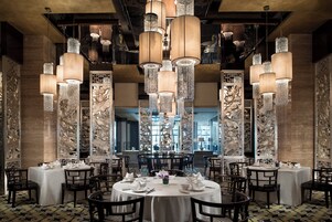 A restaurant with round tables, high ceiling chandeliers, and decorative wall panels.