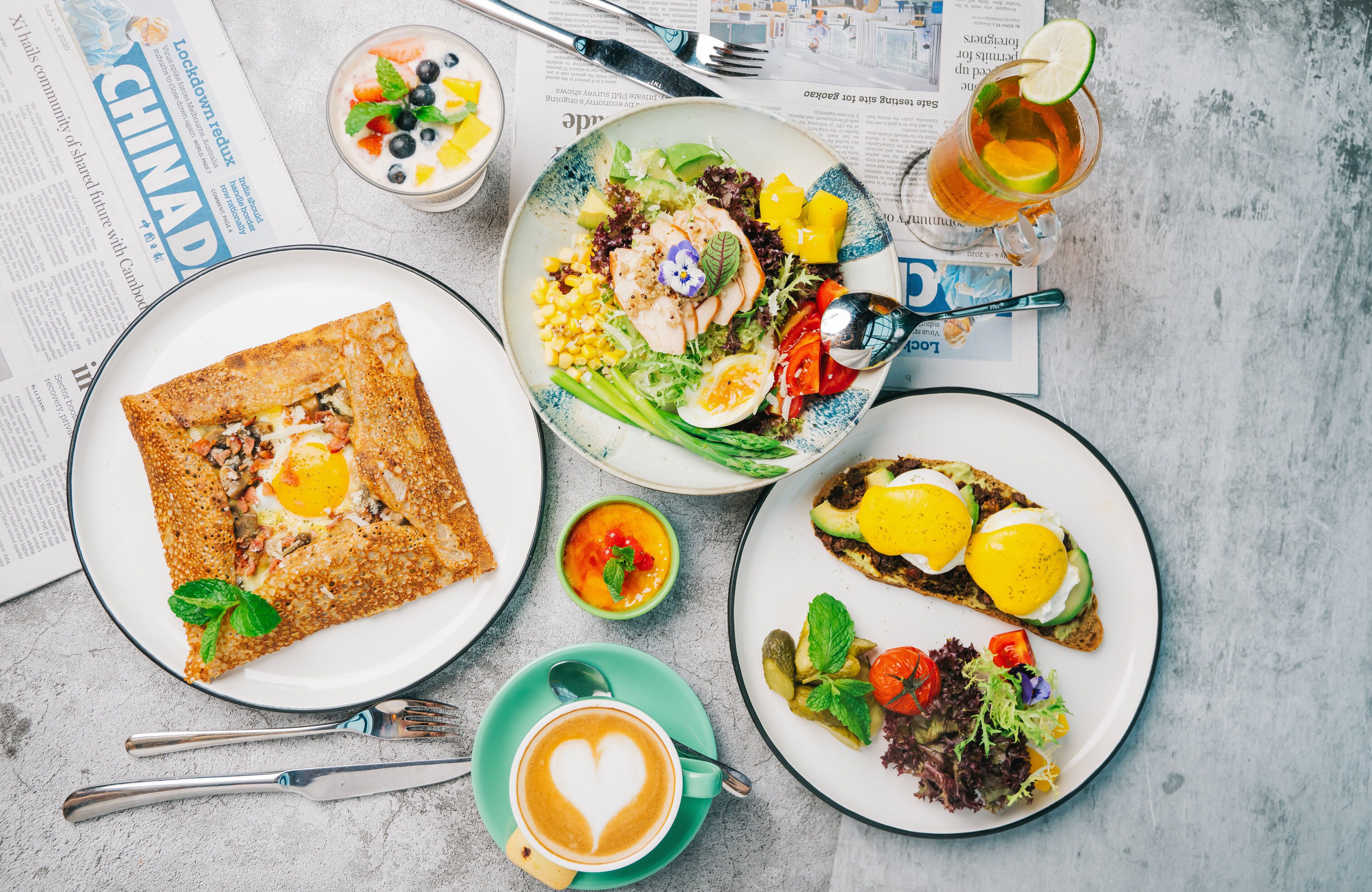 Un desayuno con diferentes platos, un periódico y una taza de café.