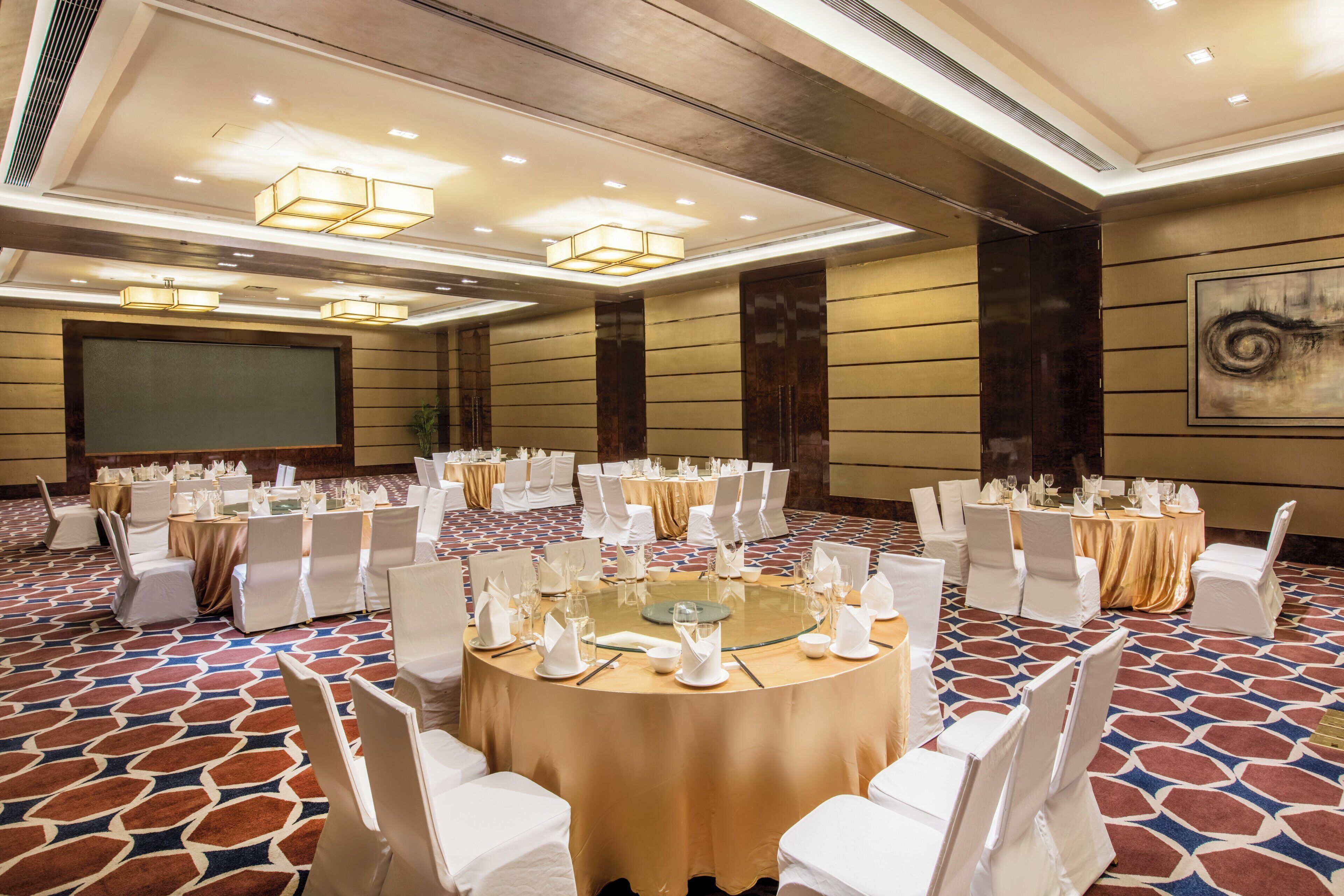 A conference room with round tables, white chairs, and a projector screen.