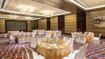 A conference room with round tables, white chairs, and a projector screen.