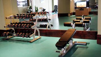 A gym with various exercise equipment including dumbbells, a bench, and a treadmill.