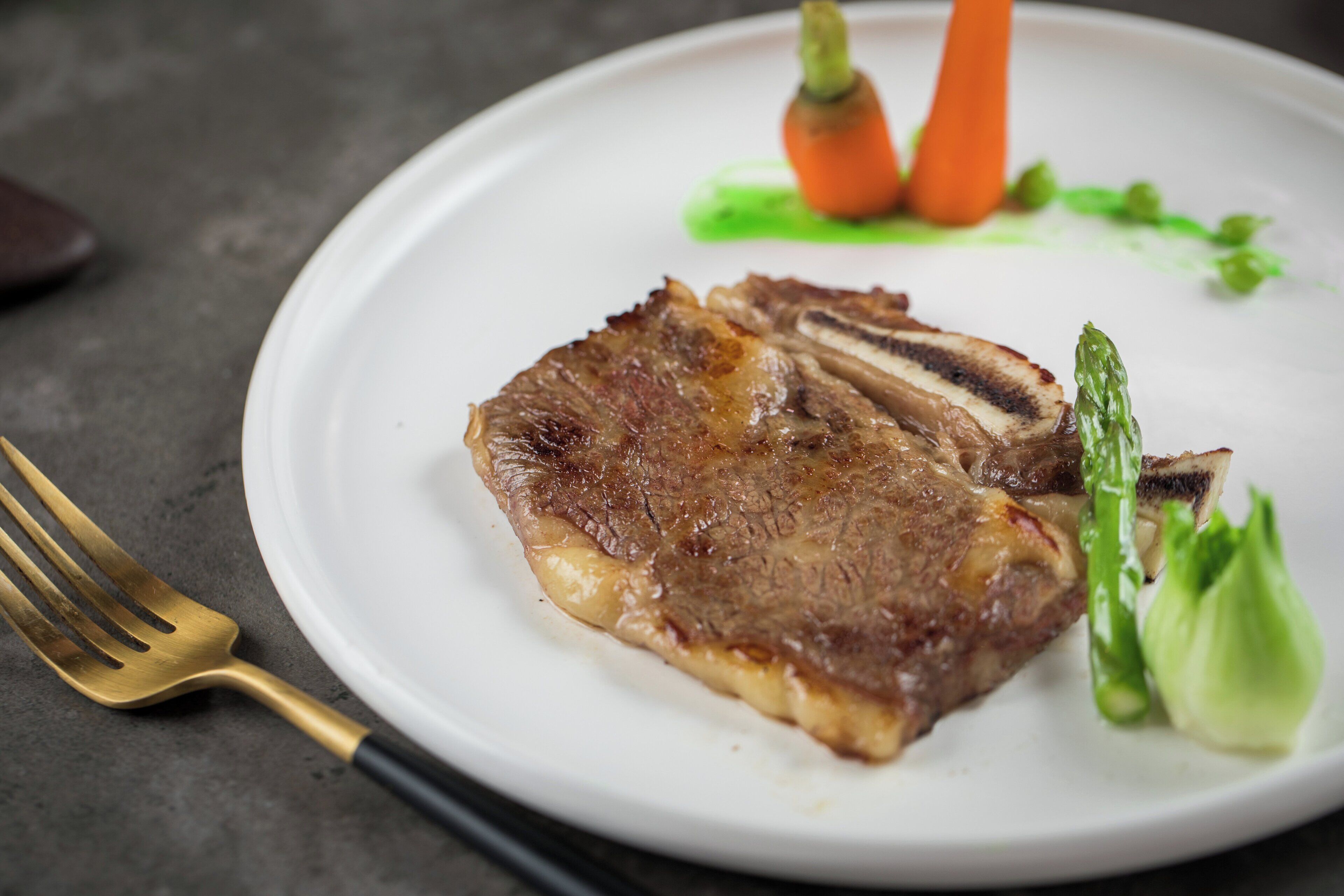 Un plato con un bistec, espárragos y zanahorias.