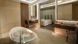 A modern bathroom with a freestanding bathtub, a vanity with a large mirror, and a separate seating area with a massage table.