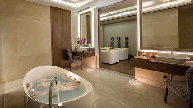 A modern bathroom with a freestanding bathtub, a vanity with a large mirror, and a separate seating area with a massage table.