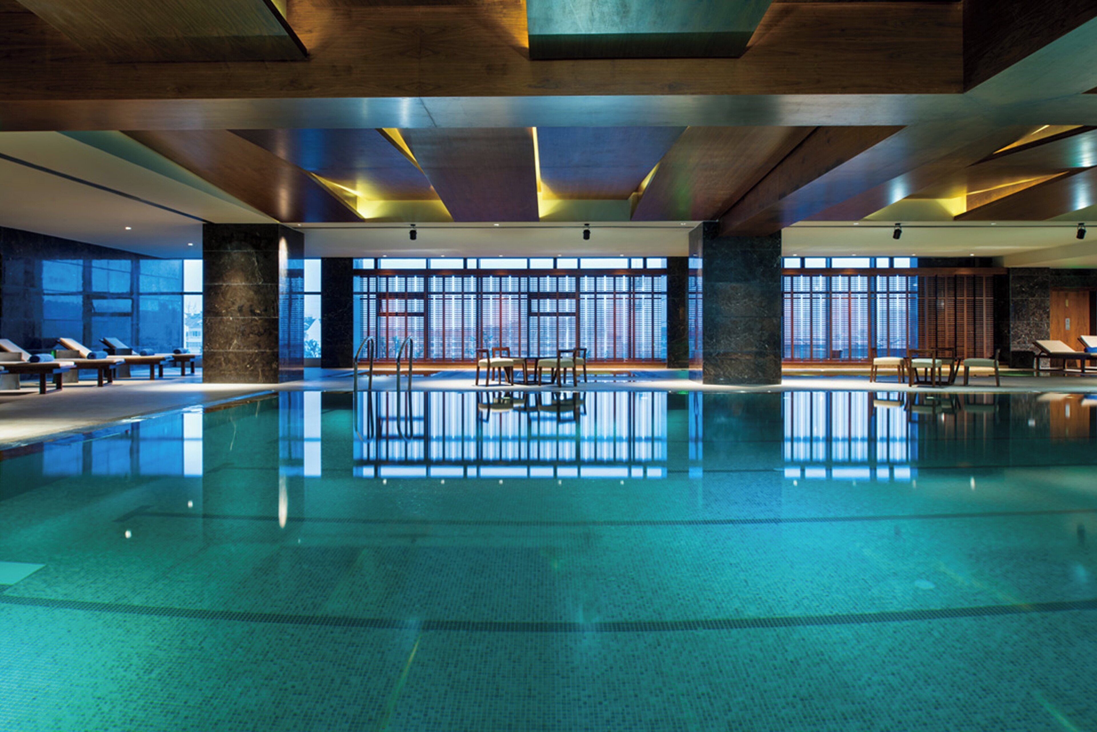 A large indoor swimming pool with clear blue water, surrounded by lounge chairs and a modern architectural design with large windows.
