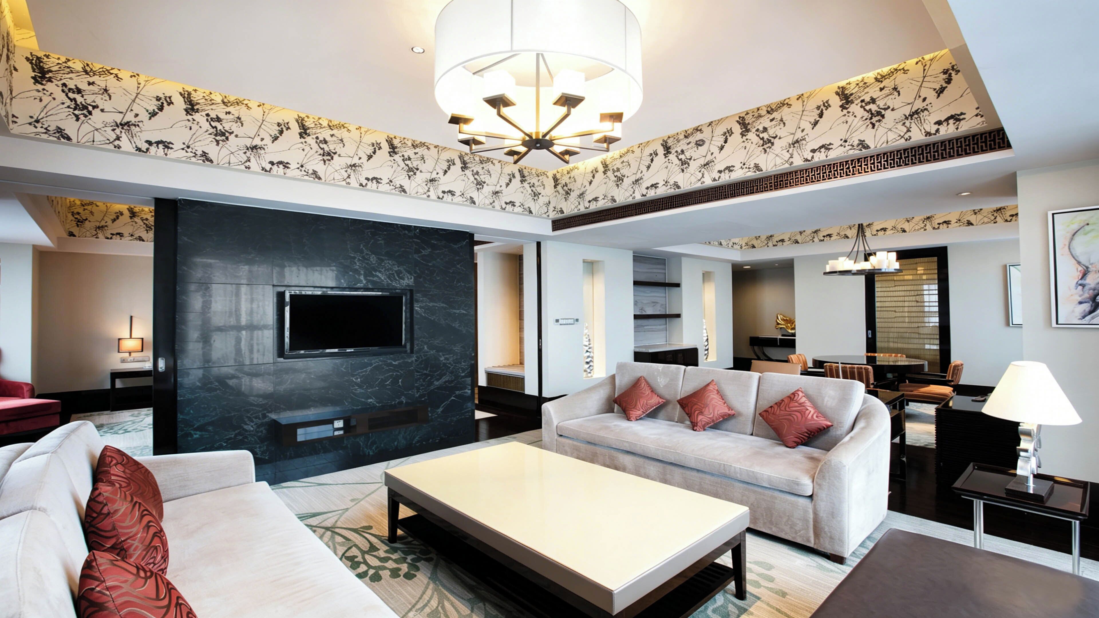 Una habitación de hotel moderna con televisor de pantalla plana, un sofá, una mesa de centro y un comedor con candelabro.