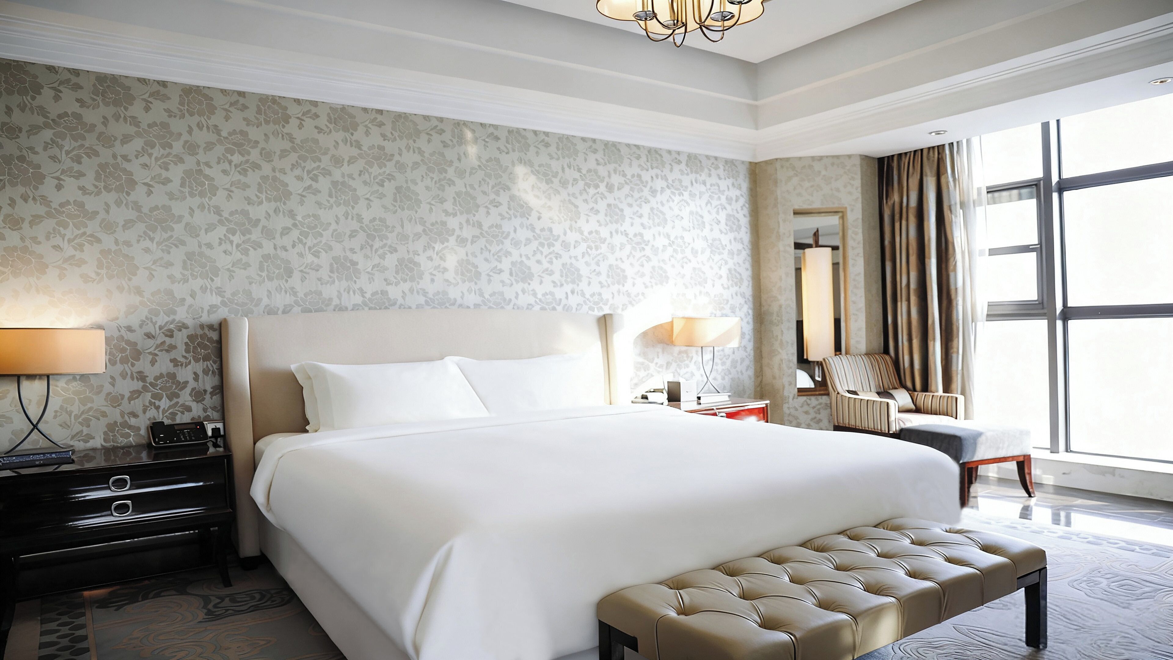 A spacious hotel room with a large bed, a bedside table with a lamp, a chair, and a large window offering a view.
