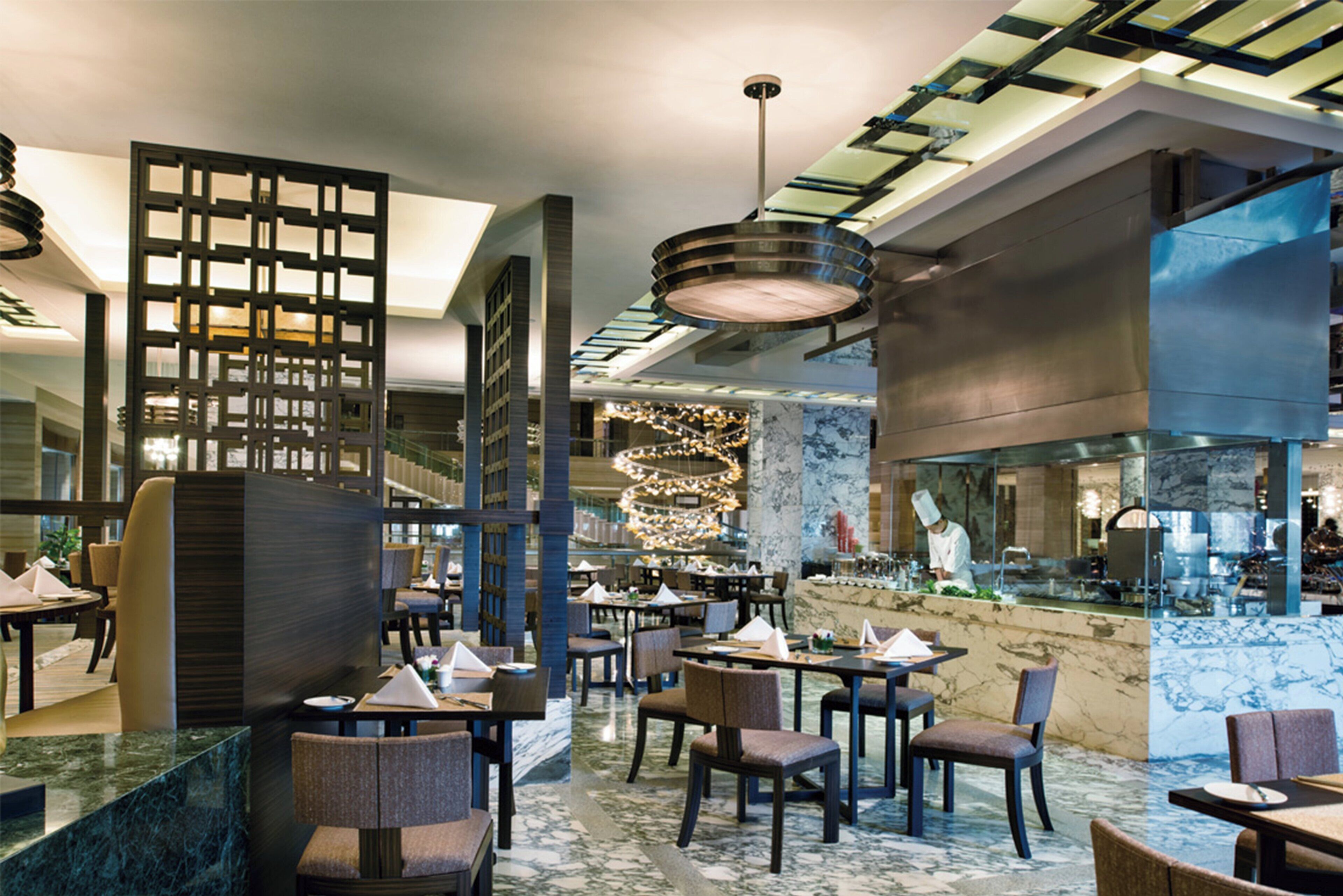 A modern restaurant with marble flooring, dark-toned chairs, and a central chandelier.