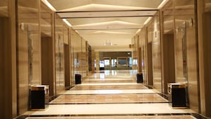 A modern hotel corridor with marble flooring, glass doors, and a digital elevator display.