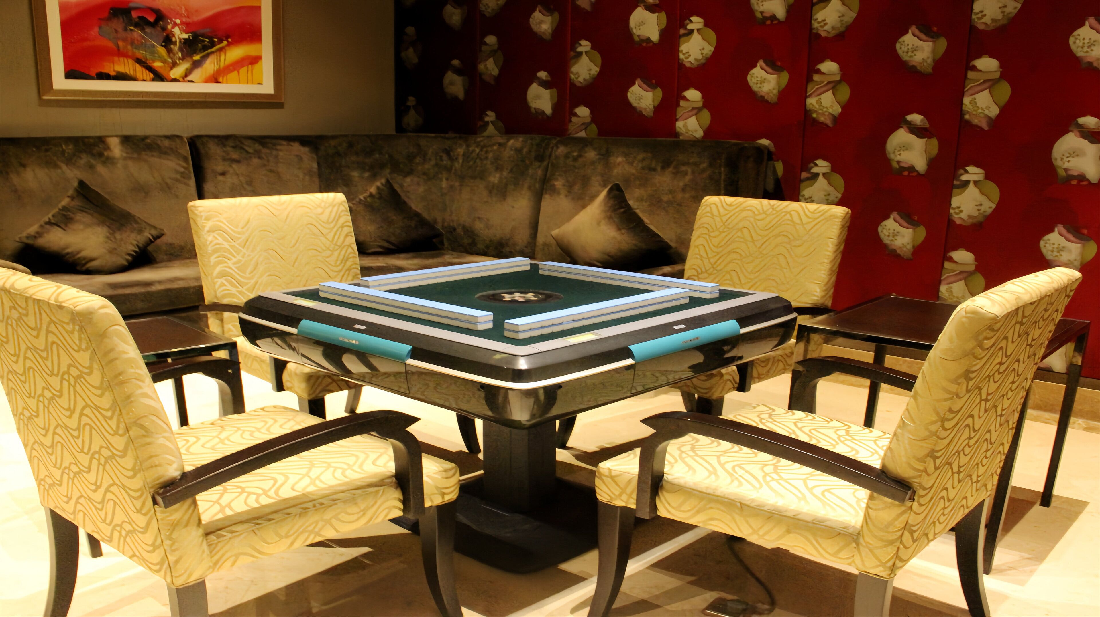 Un comedor con una mesa cuadrada rodeada de cuatro sillas, un sofá al fondo y una pared con diseño.