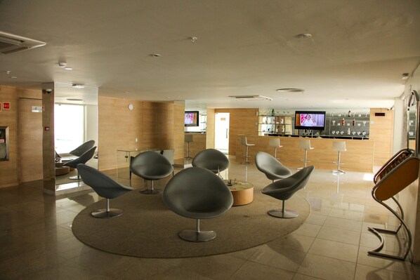 Un área de espera moderna con sillas contemporáneas, un bar con televisor y un diseño limpio y minimalista.