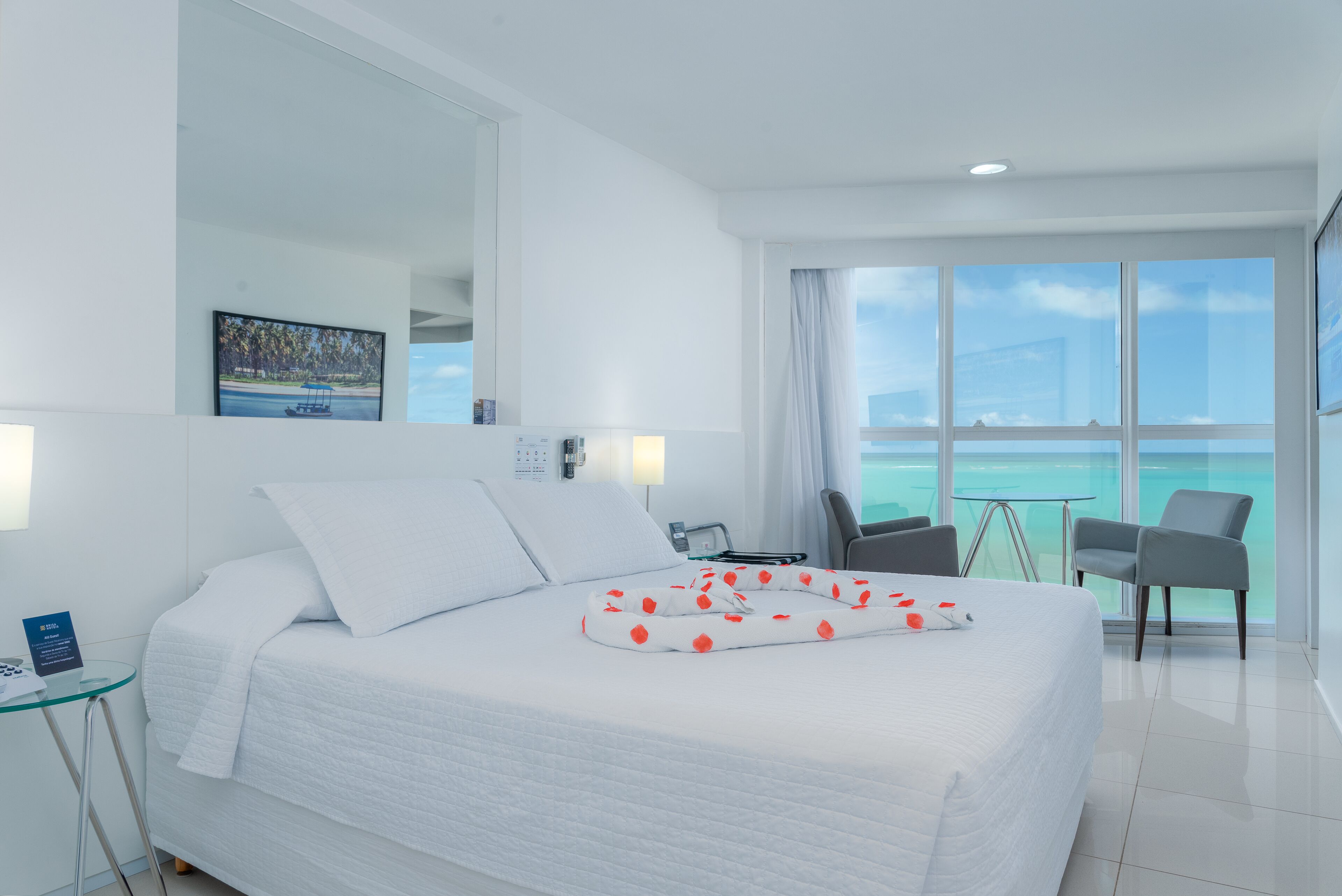 Quarto de hotel moderno com uma cama grande, uma escrivaninha e vista para o oceano.