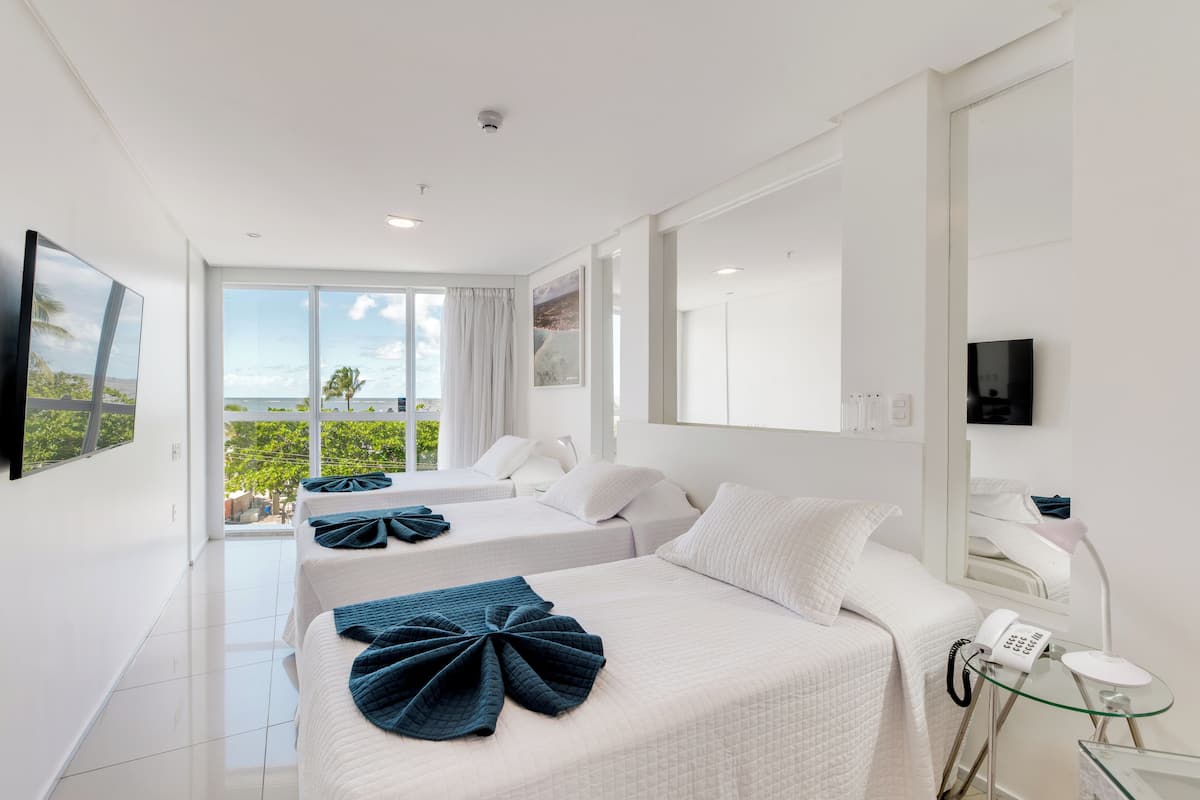 A hotel room with two beds, a large window with a view, a flat-screen TV, and a telephone.