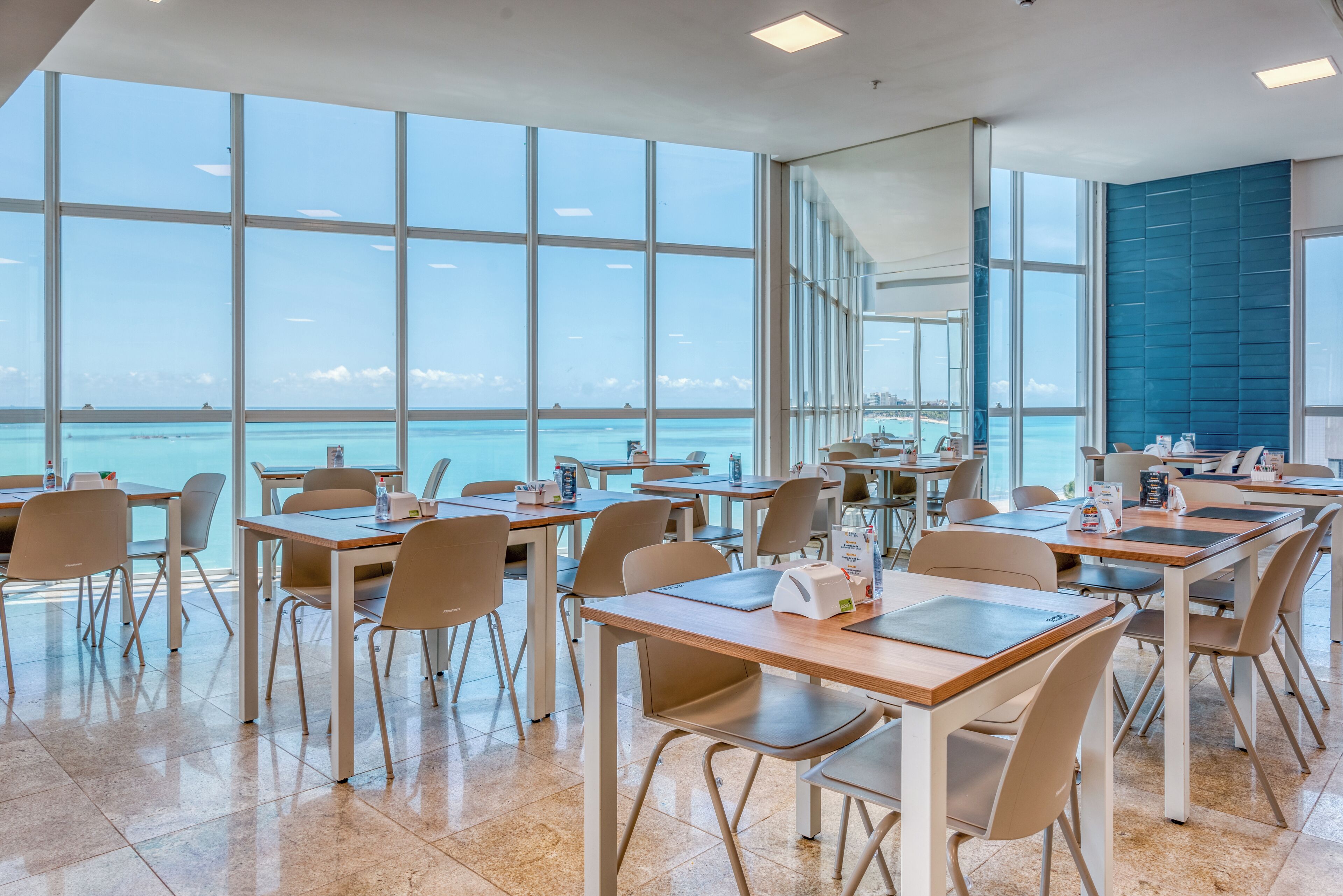 A modern dining area with large windows overlooking a body of water, featuring clean lines and a minimalist design.