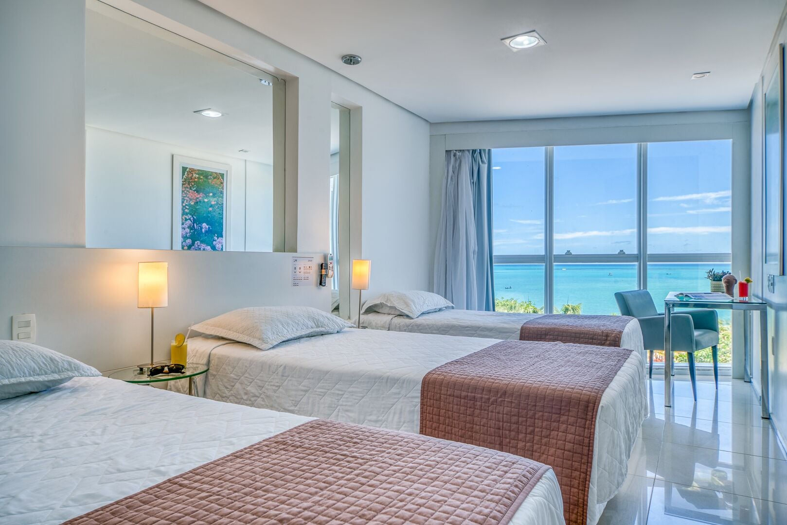 Habitación de hotel con dos camas, un escritorio y vista al océano.