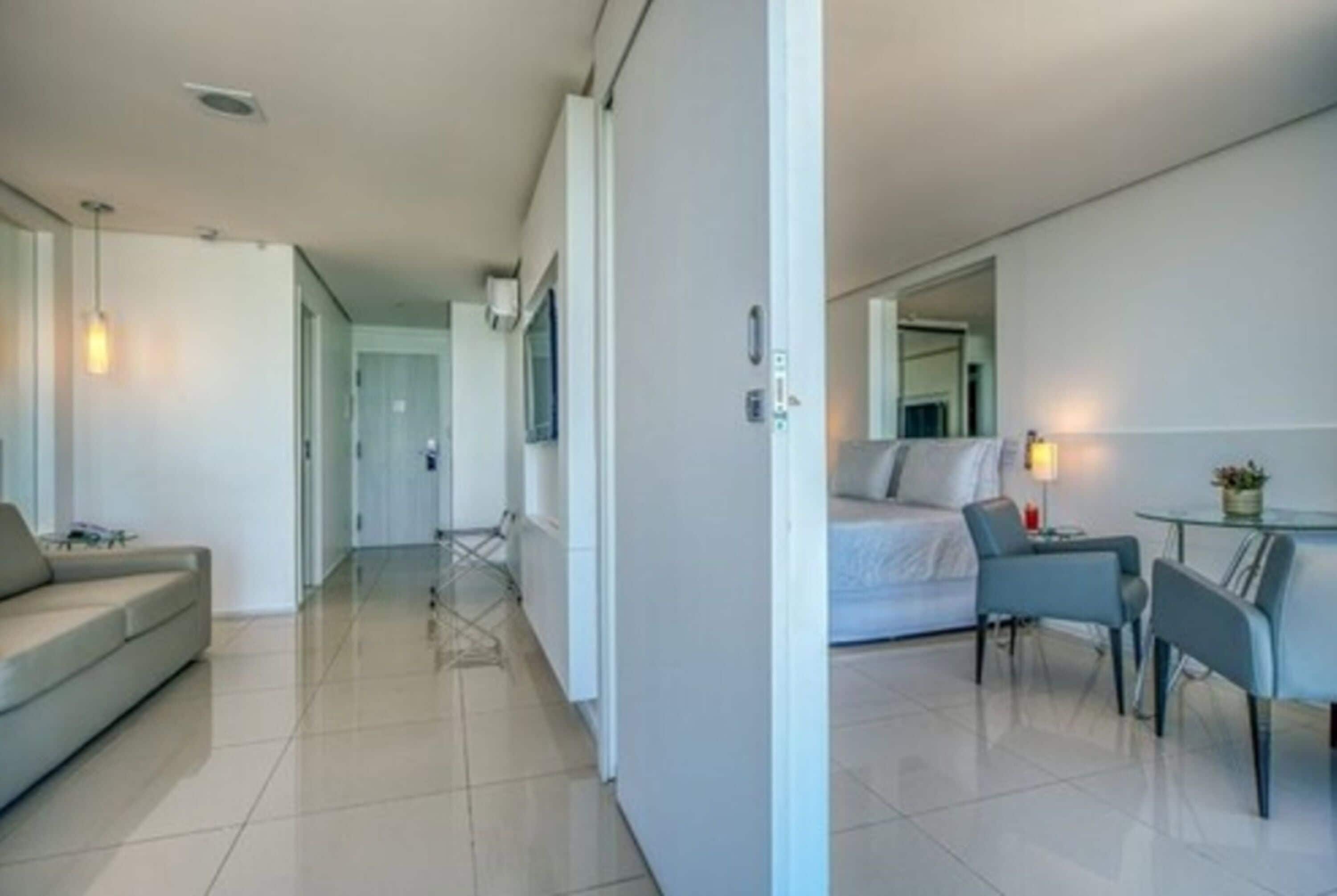A modern, well-lit living room with a sofa, a dining area with a table and chairs, and a large mirror on the wall.
