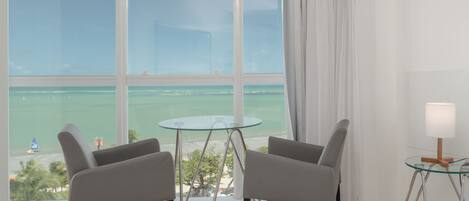 Una habitación moderna con un ventanal grande, dos sillas grises, una mesa de vidrio y una lámpara.