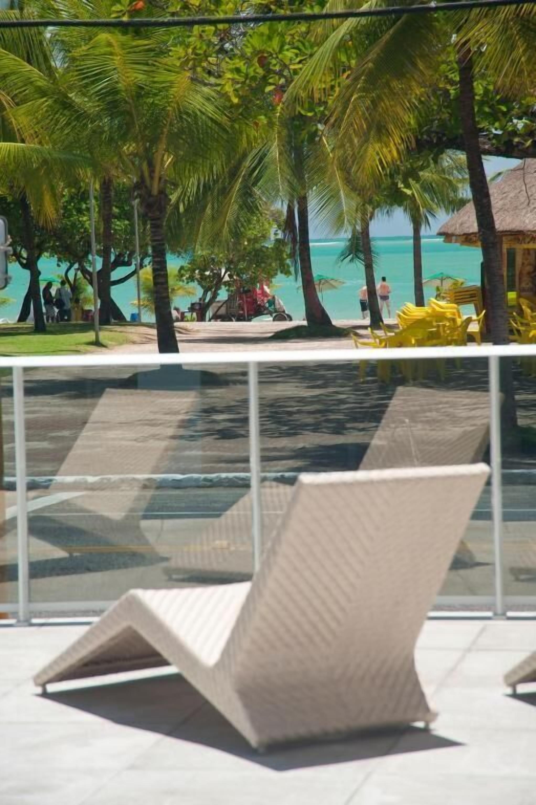 A poolside area with a lounge chair, palm trees, and a view of the beach.