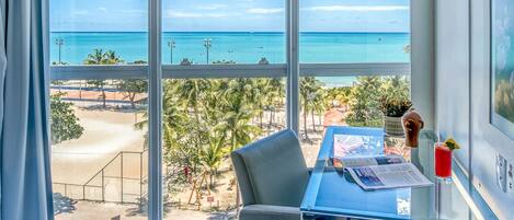 A hotel room with a large window offering a view of the beach and ocean.