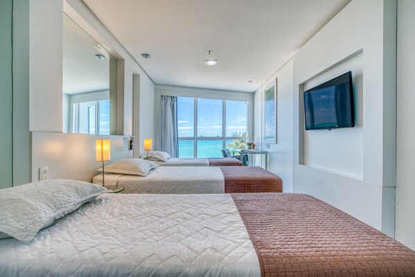Habitación de hotel con dos camas, un escritorio, un televisor y vista al mar.