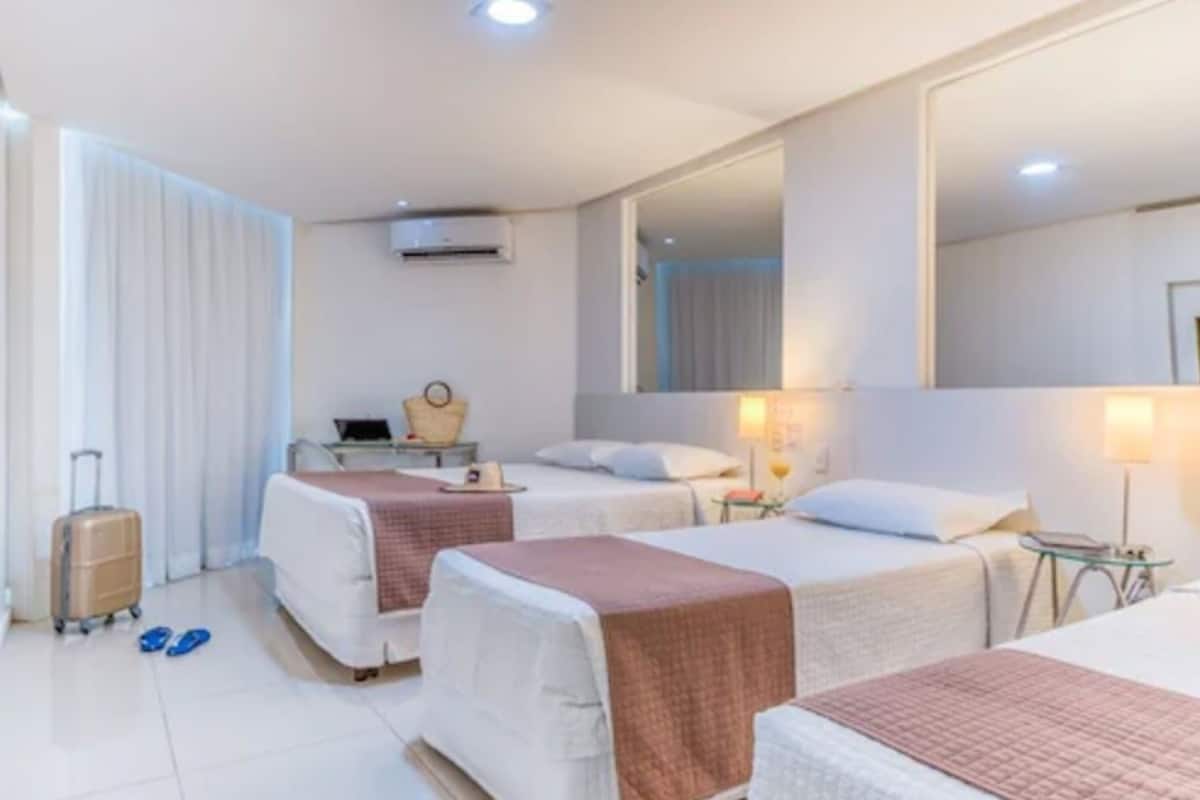 A hotel room with two beds, a desk, a chair, a lamp, and a suitcase.