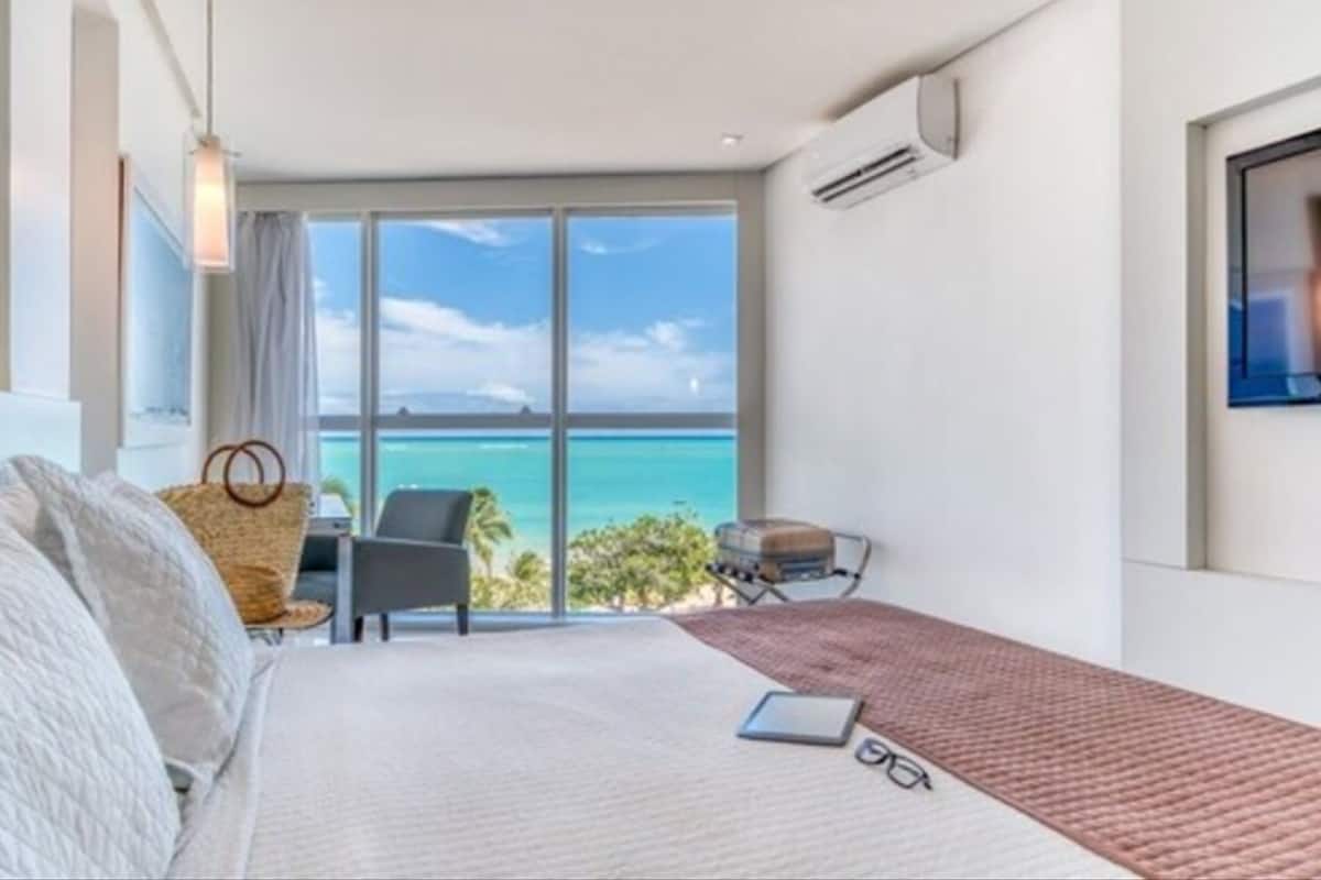 A modern hotel room with a large window offering a view of the ocean.