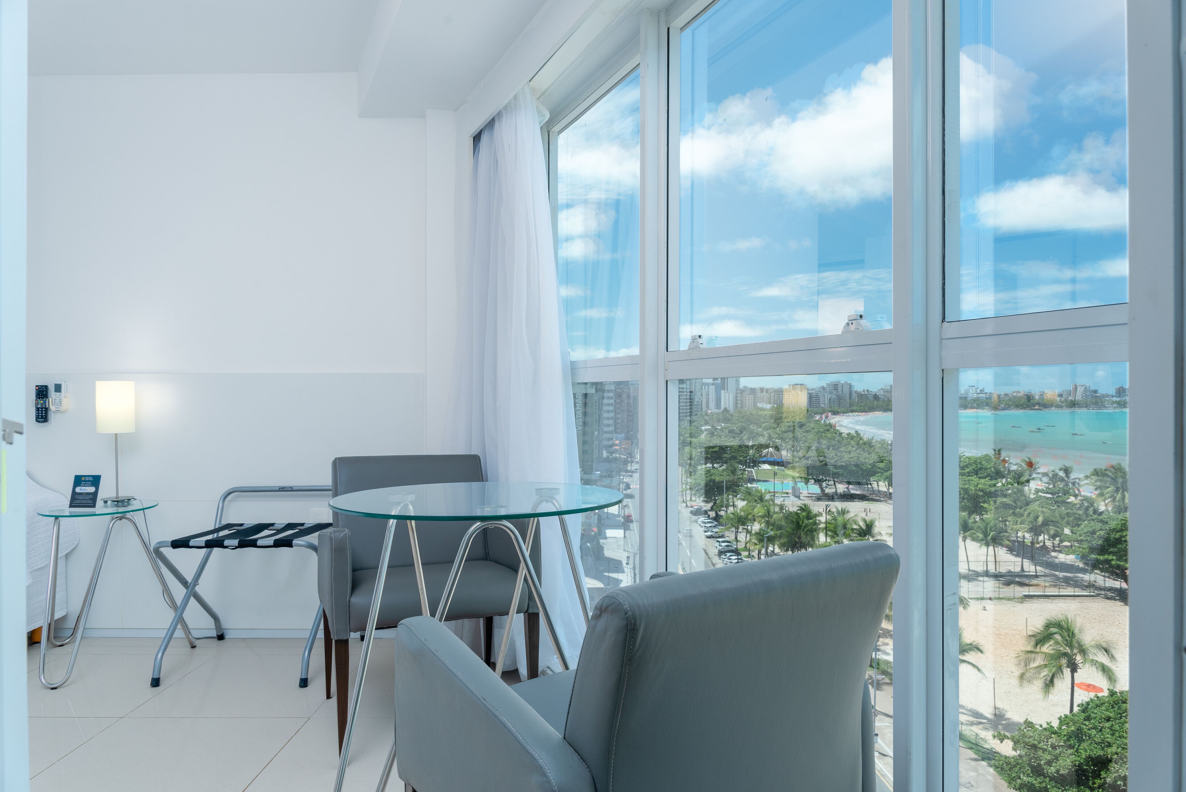 A modern hotel room with a large window offering a view of a beach and cityscape.