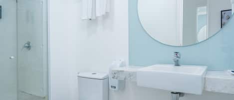 A modern bathroom with a glass shower enclosure, a white toilet, a sink with a marble countertop, and a round mirror.