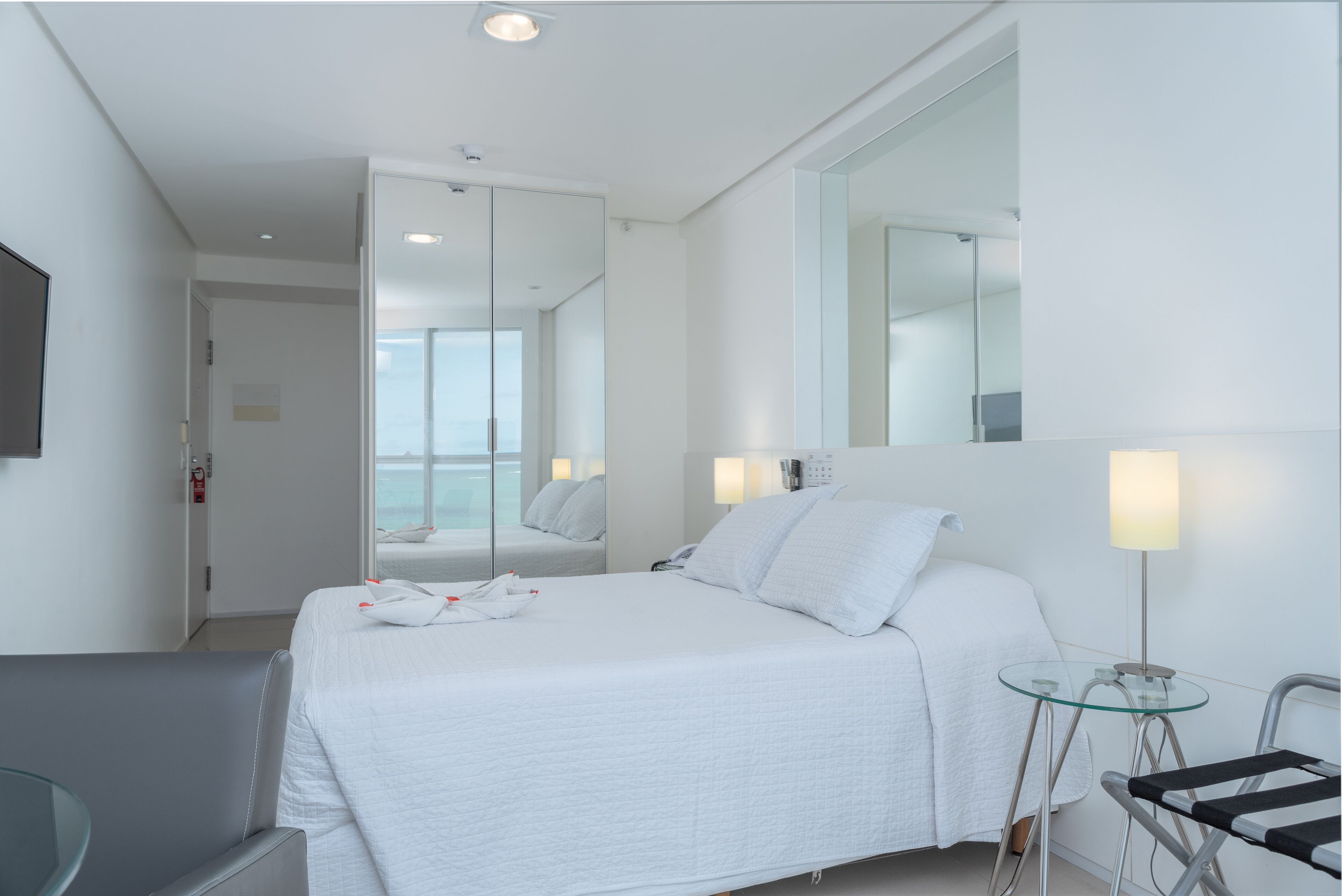 Una habitación de hotel moderna con una cama grande, una mesa de vidrio, una silla y un espejo.