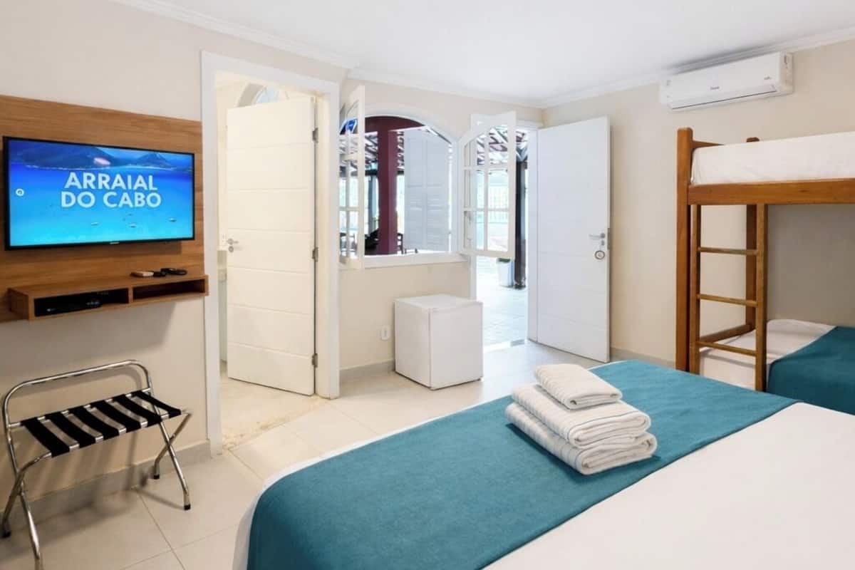 A hotel room with a bed, a TV, a bunk bed, a small table, and a chair.