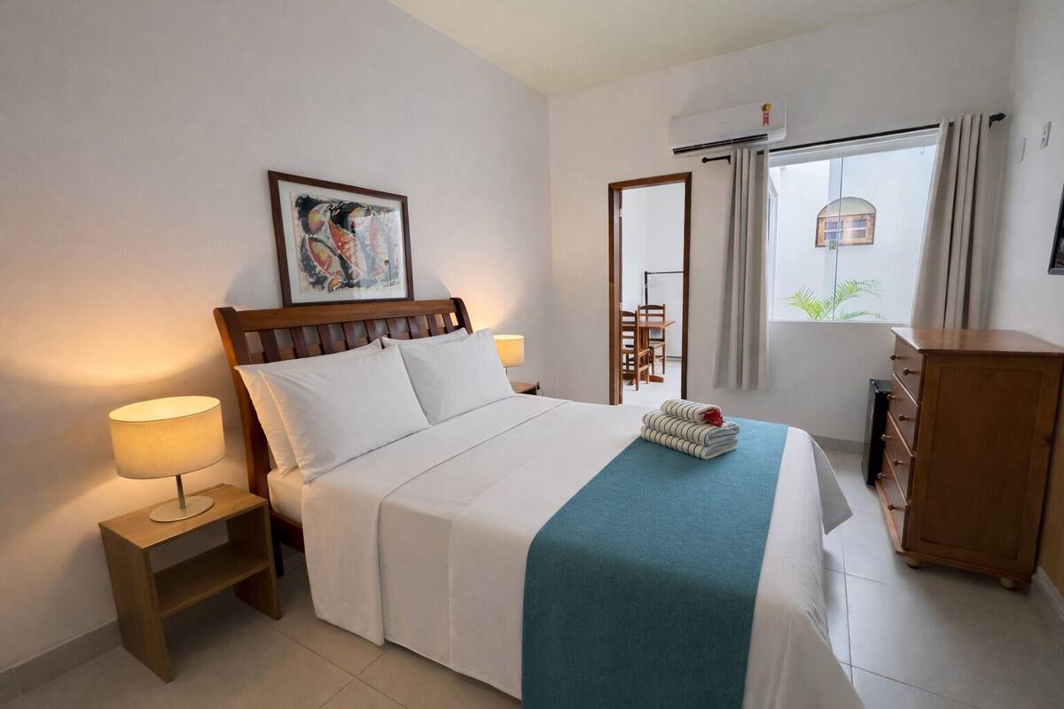 A neatly arranged hotel room with a bed, bedside lamps, a dresser, and a window with curtains.