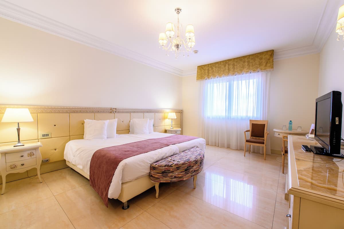 A hotel room with a large bed, bedside tables, a television, and a desk.
