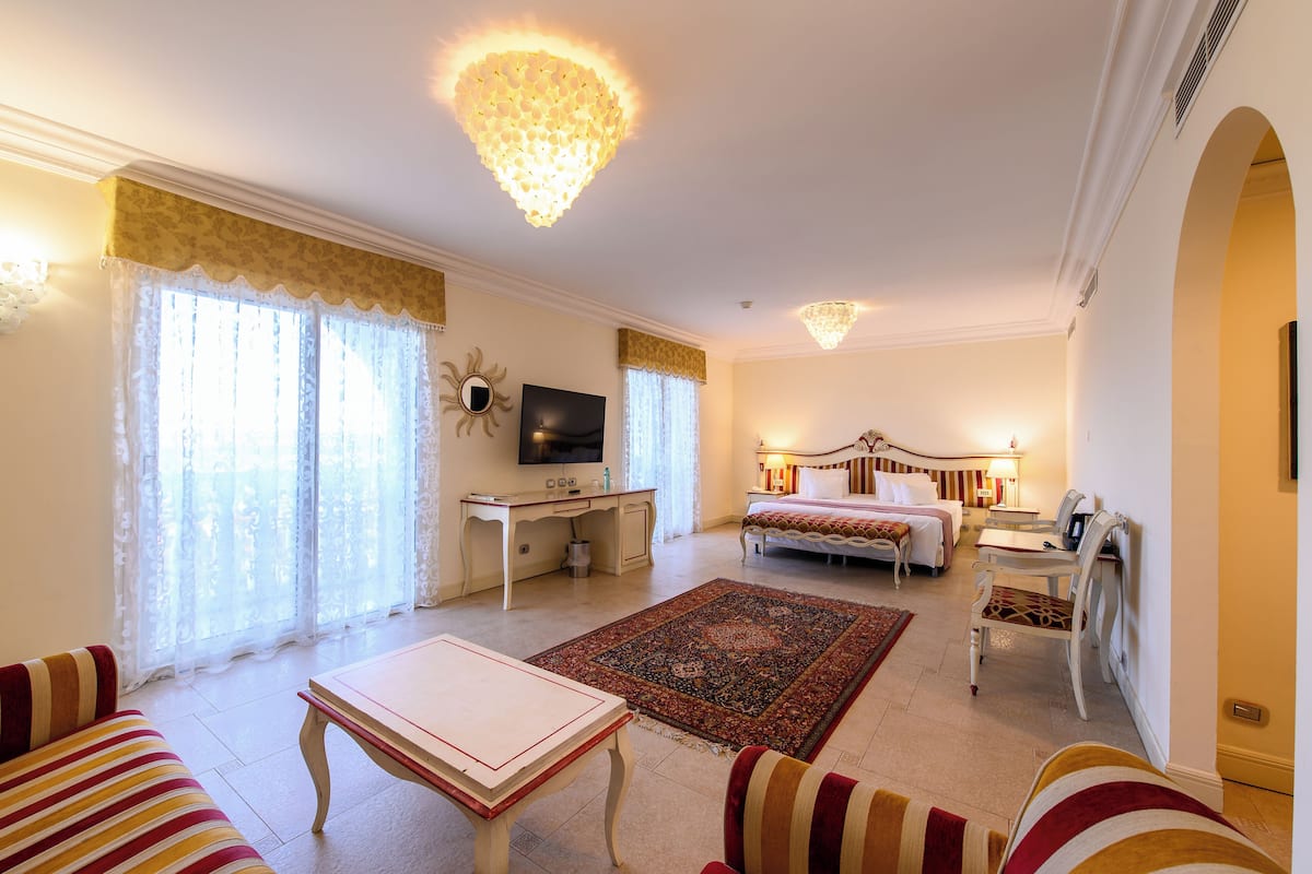 A spacious hotel room with a large bed, a desk, a television, and a chandelier.