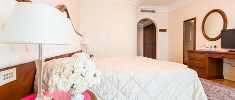 Una habitación de hotel con una cama, un escritorio, una silla, una lámpara, un espejo y un jarrón con flores.